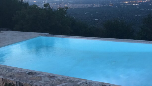 Una piscina rectangular con borde de piedra, rodeada por un muro de piedra y cactus.