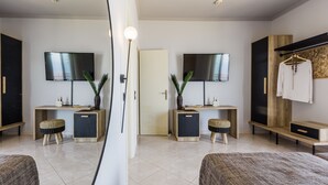 Ett modernt hotellrum med en stor spegel, två tv-skärmar, en garderob, ett sängbord och en säng.