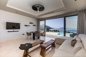 A modern living room with a large TV, a dining table, and a sofa. - Villa with private pool - endless sea view / mountain view - Villa Di Capri (Unknown)