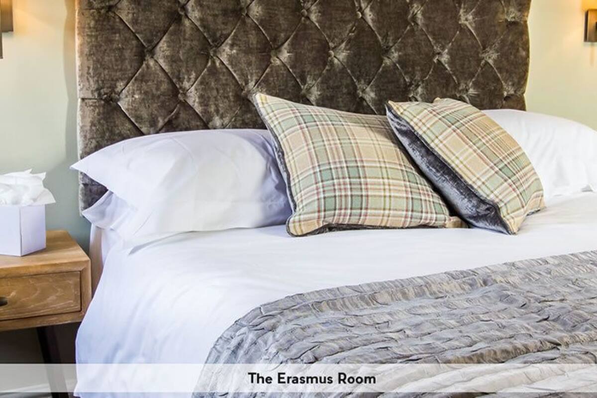 A neatly made bed with a tufted headboard, two pillows, a bedside table with a tissue box, and a nightstand.