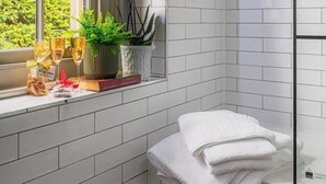 Een badkamer met witte metro tegels, een raam met uitzicht op groen, een plant en een stapel witte handdoeken.
