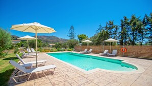 Una piscina rectangular con borde de baldosas, rodeada de sillas de descanso y sombrillas.