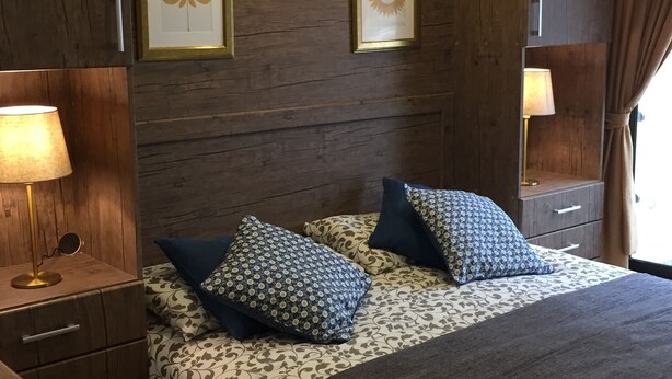 A bedroom with a large bed, two bedside lamps, a wooden headboard, and two framed wall art pieces.