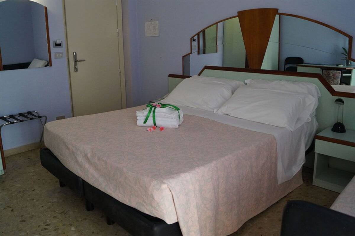 A hotel room with a bed, a bedside table, a mirror, and a door.