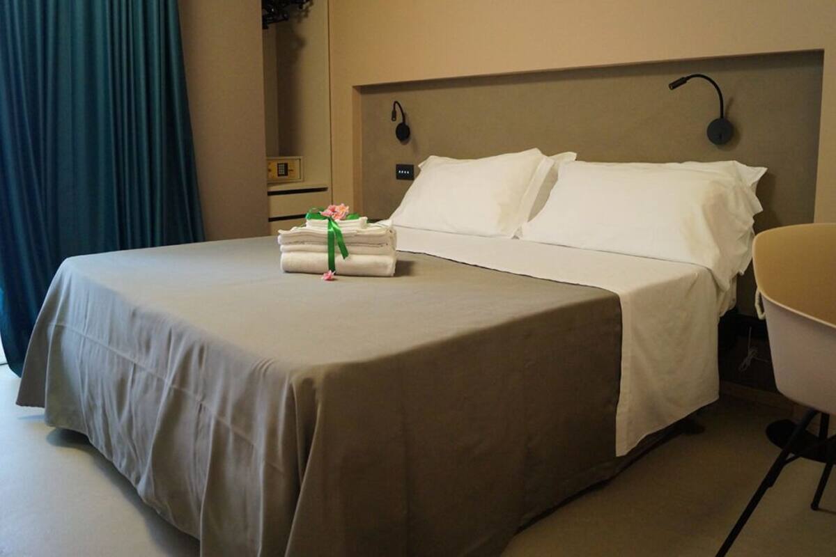 A hotel room with a neatly made bed, a chair, and a small table with folded towels and a flower.