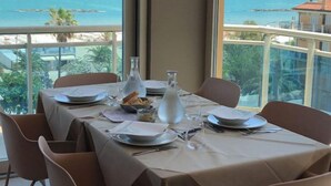A dining table set for four with a view of the sea through large windows.