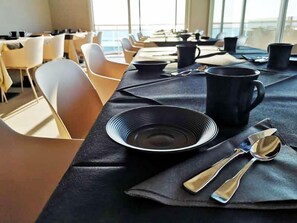 A dining area with tables set for service, chairs, and a view of the sea through large windows.