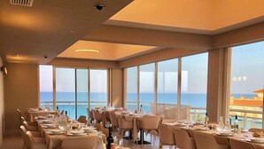 A dining area with tables set for service, large windows offering a view of the sea, and a modern ceiling design.