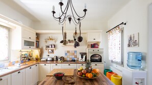 Una cocina moderna con armarios blancos, una isla de madera, una lámpara de araña y un dispensador de agua.