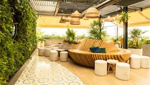 A modern outdoor seating area with a wooden sofa, ottomans, and hanging planters.