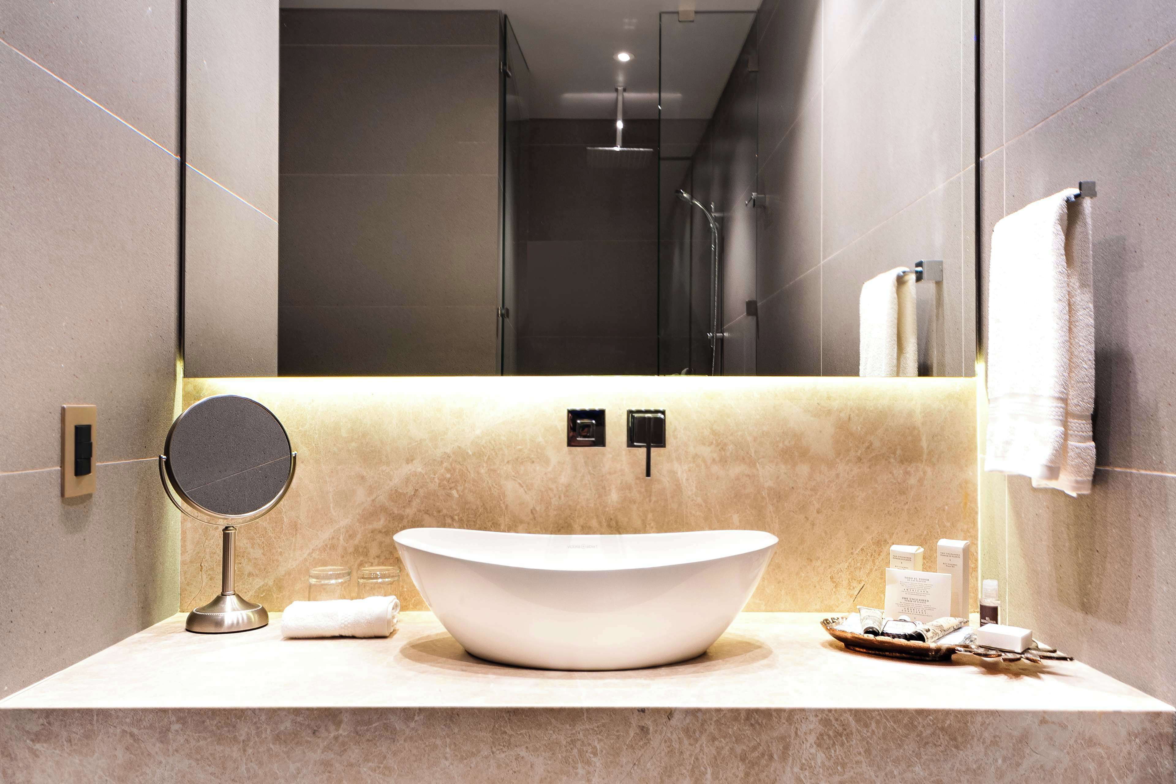 A modern bathroom with a large sink, a round mirror, and a towel rack.
