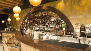 A bar area with a wooden counter, multiple seating options, and a variety of bottles and glasses on shelves.