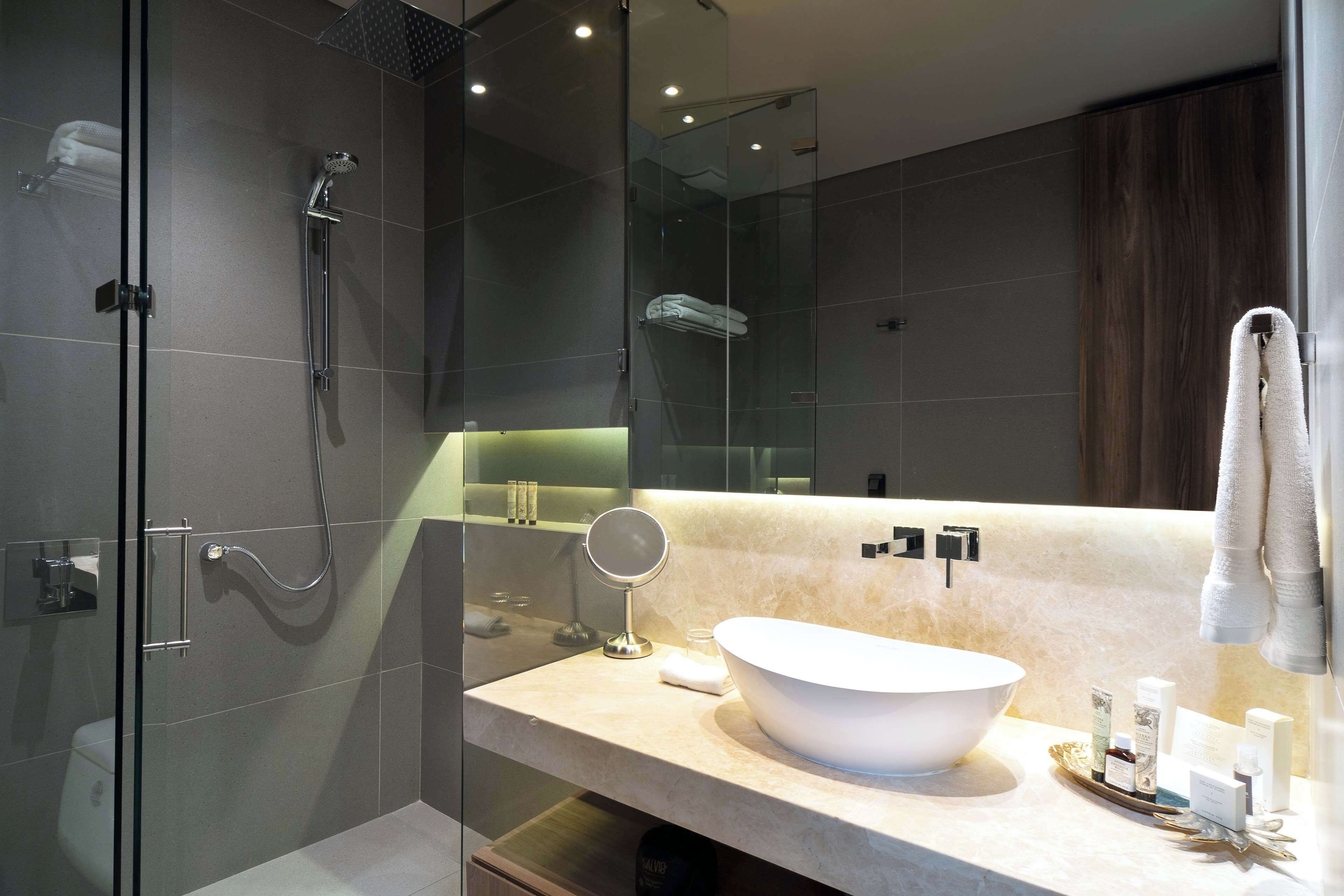 A modern bathroom with a glass shower enclosure, a large mirror, and a vanity with a white sink and toiletries.