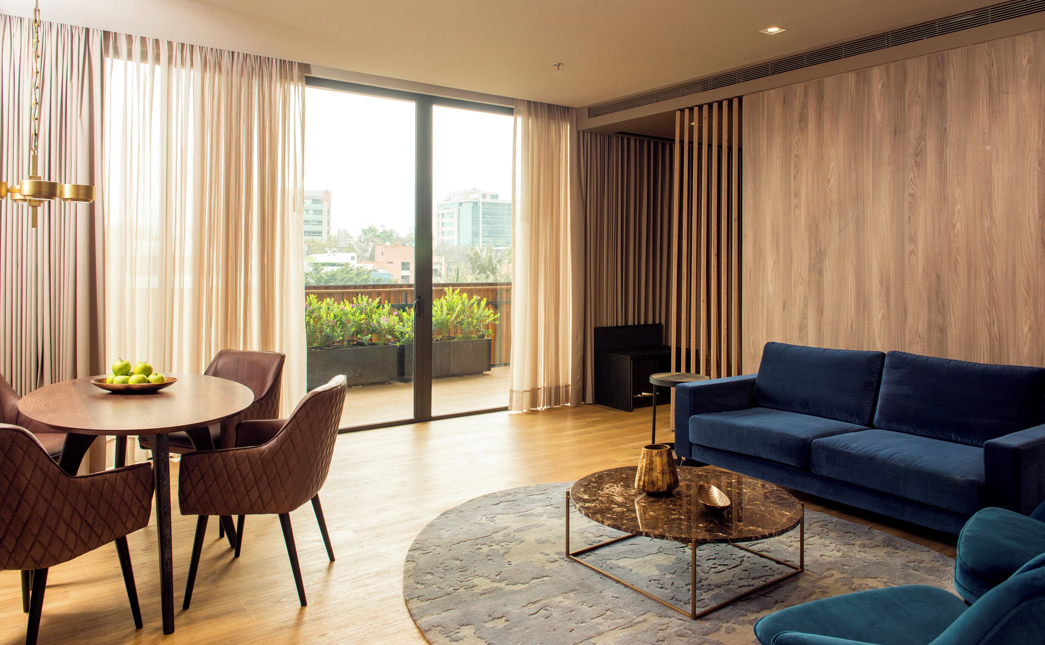 A modern living room with a blue sofa, a round coffee table, and a dining area with a wooden table and chairs.