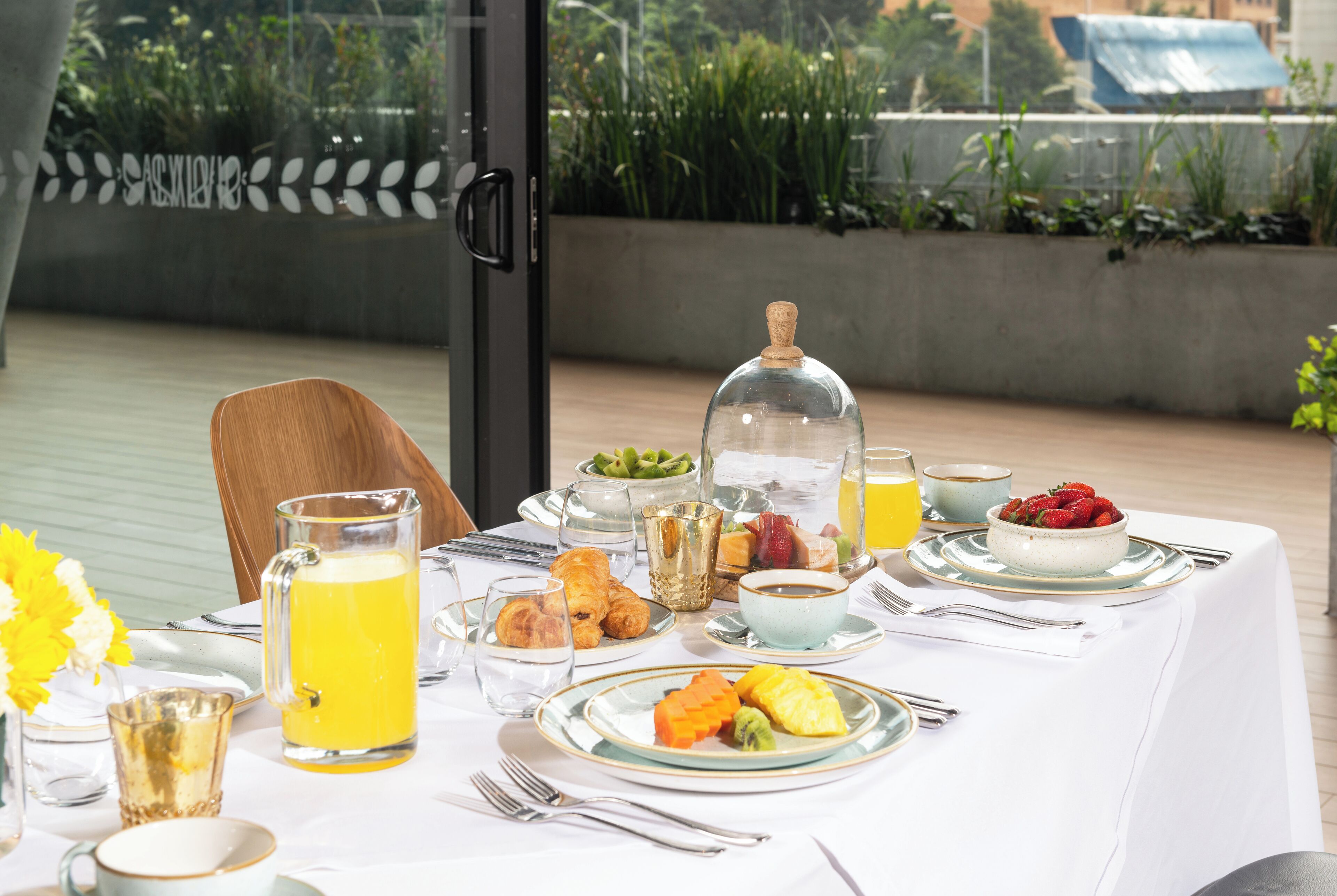 A breakfast table set with various dishes, including fruits, pastries, and beverages, on a white tablecloth.