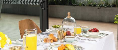 A breakfast table set with various dishes, including fruits, pastries, and beverages, on a white tablecloth.