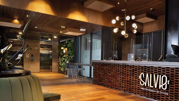 A modern reception area with a wooden reception desk, a green sofa, and a plant wall.