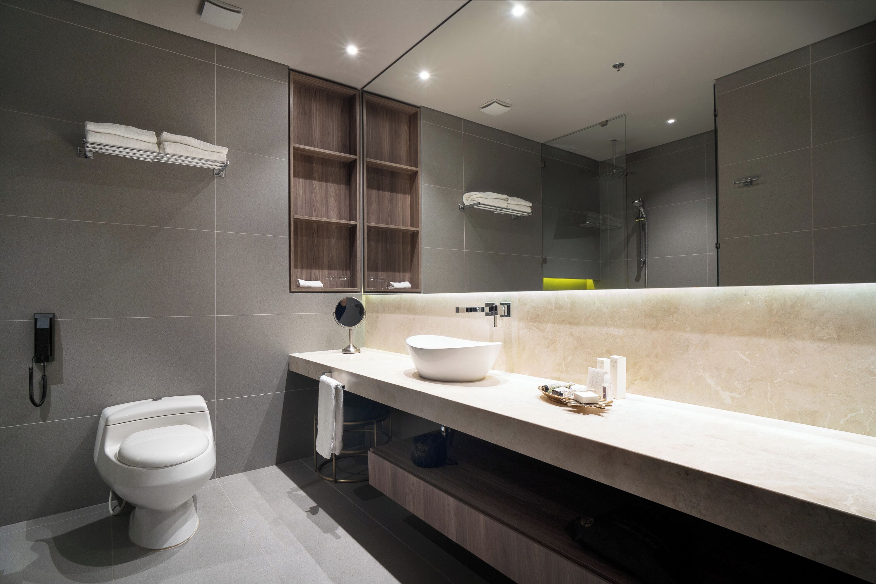 Et moderne badeværelse med toilet, vaskebord med stort spejl og bruseområde.