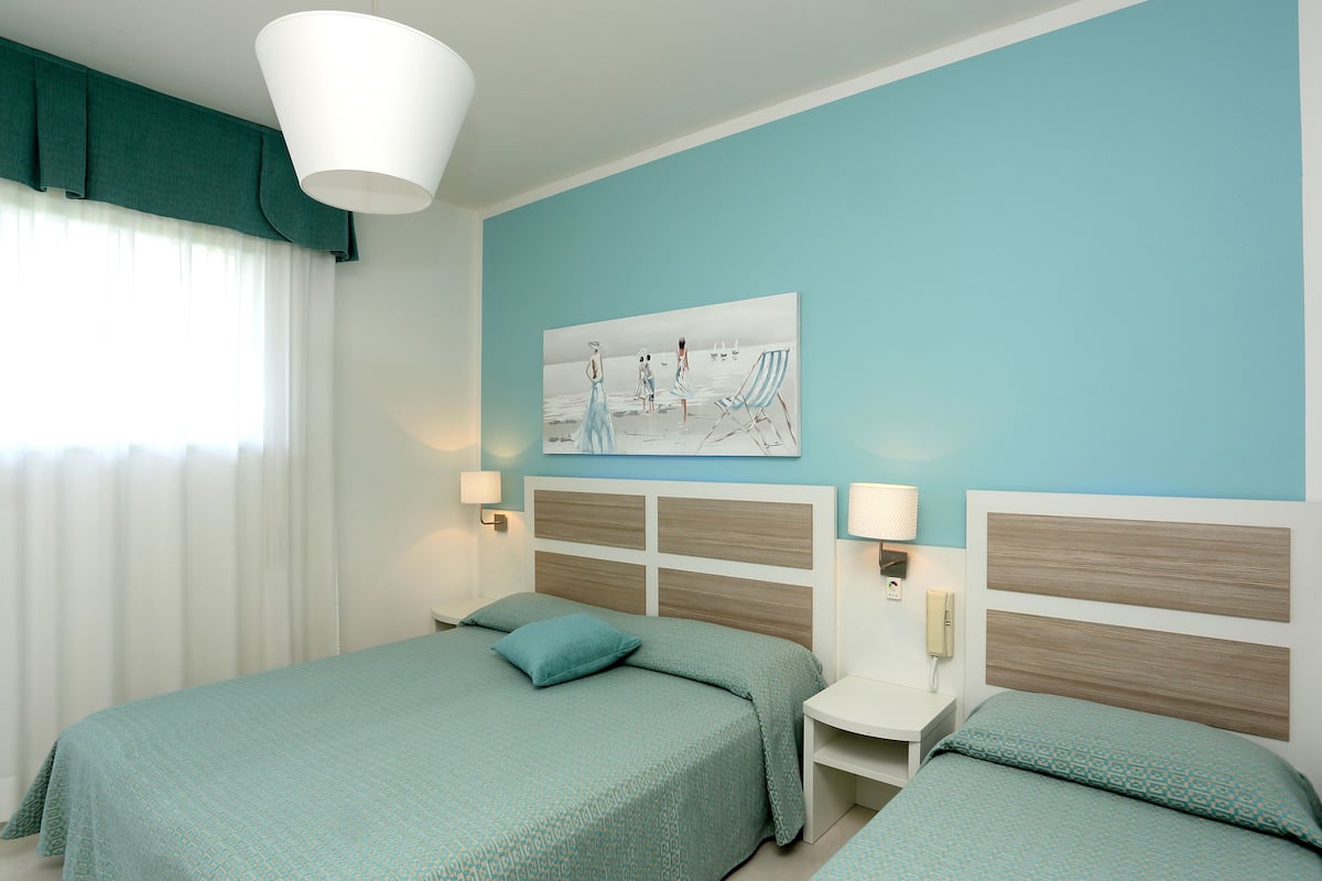 Une chambre d’hôtel avec deux lits, un tableau au mur et une fenêtre avec des rideaux.