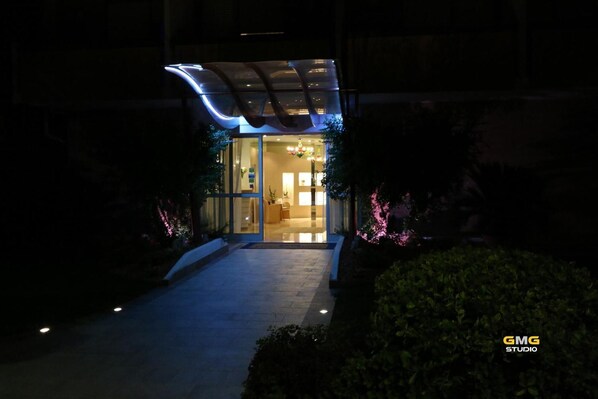 A hotel entrance with a glass facade, a reception area, and a pathway leading to the entrance.