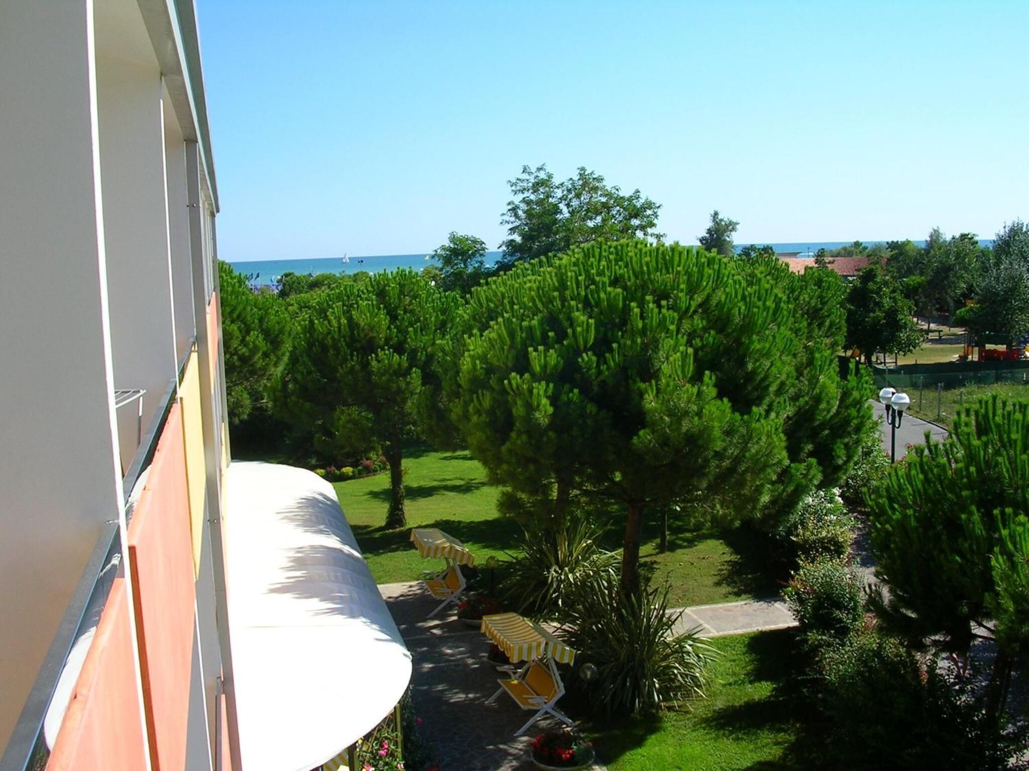 Ein Balkon mit Blick auf einen gepflegten Garten und einen wolkenlosen, blauen Himmel.
