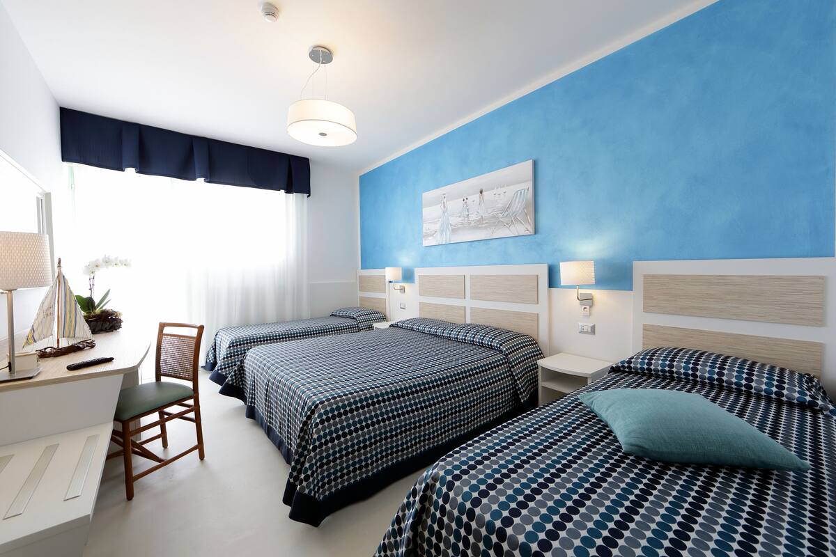 Une chambre d’hôtel avec deux lits, un bureau, une chaise et une fenêtre avec des rideaux.