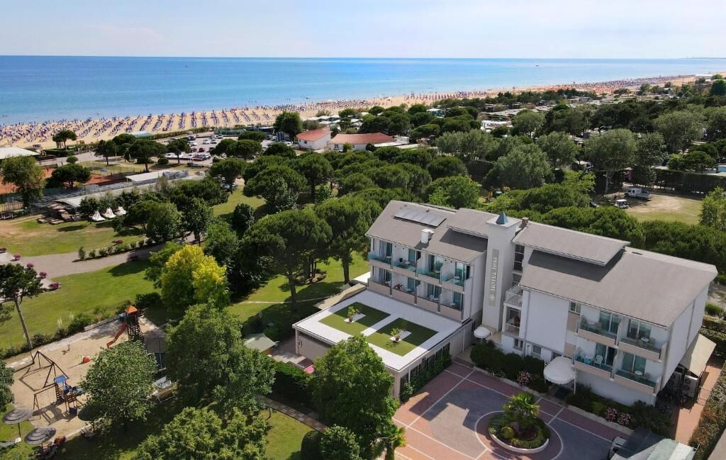 Ein modernes Hotel mit Dachterrasse, umgeben von üppiger Bepflanzung und Blick auf einen Strand.