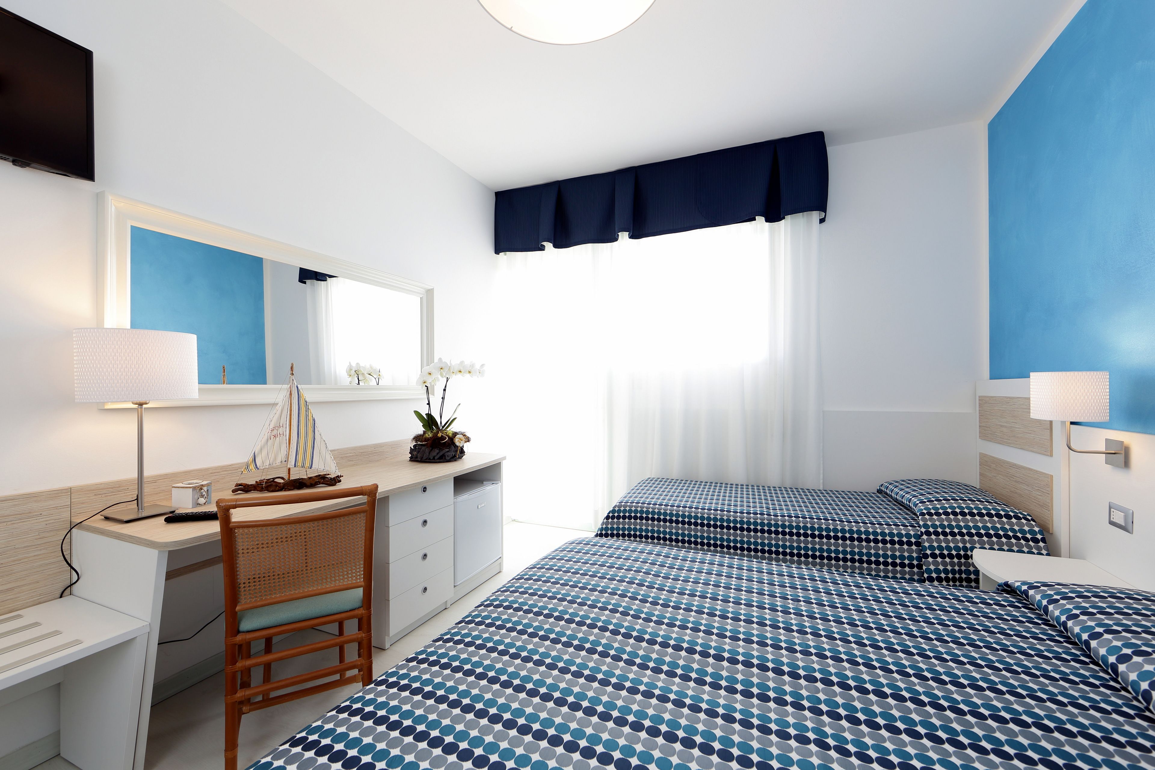 A bedroom with a bed, a desk, a chair, a dresser, and a window with curtains.