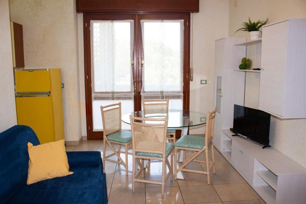 A compact living space with a blue sofa, a dining table with chairs, a television, and a small kitchen area with a yellow refrigerator.