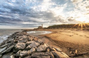 A beach with a rocky shoreline, a lighthouse, and a sunset.
