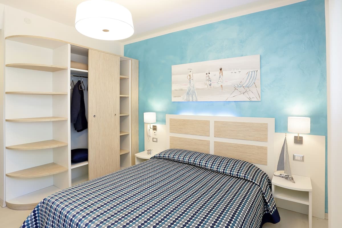 Une chambre à coucher comprenant un lit, une armoire, une table de chevet et une lampe fixée au mur.