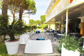 Un'area patio esterna con posti a sedere, piante in vaso e un edificio sullo sfondo.