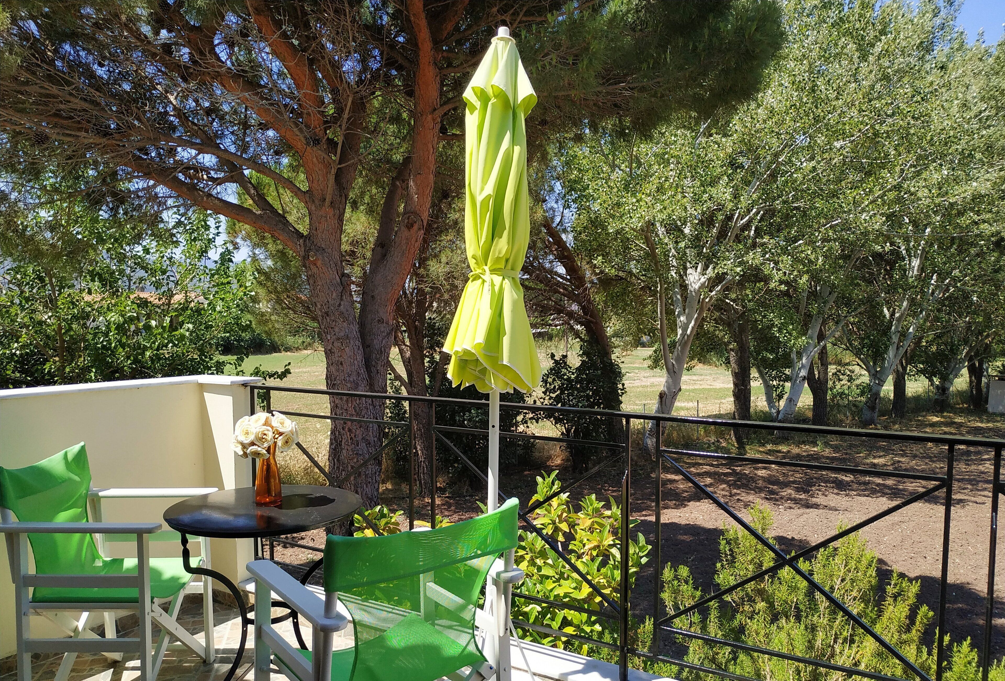 A balcony with a green chair, a small table with a vase of flowers, and a yellow umbrella.
