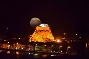 Un edifici amb una estructura blanca a la part superior, il·luminat per llums artificials, amb una gran lluna al fons.