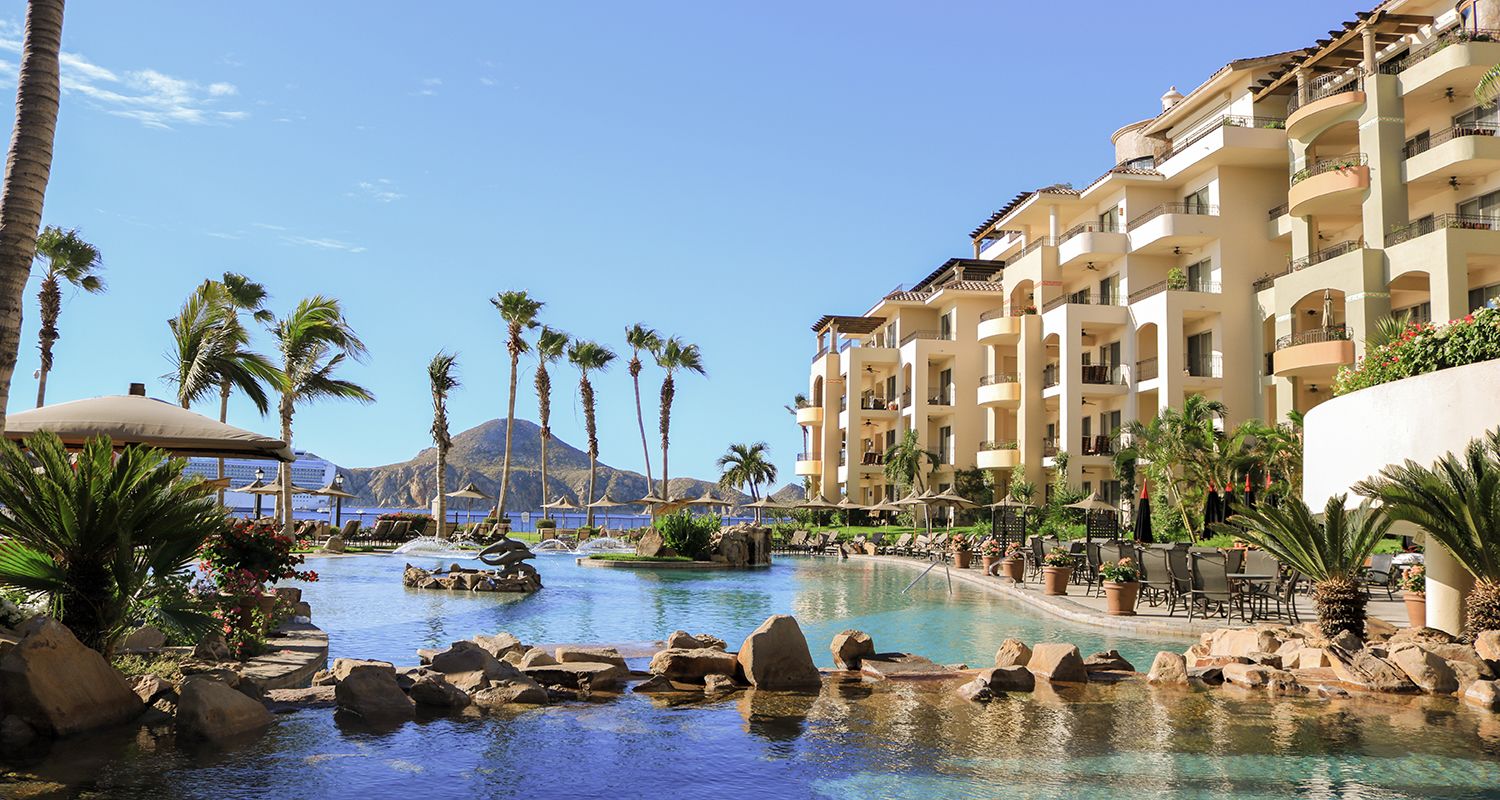 Un resort con una piscina grande, palmeras y una montaña al fondo.