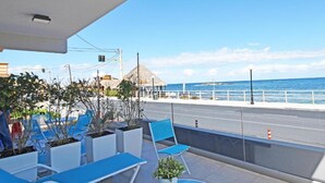 En balkong med blå loungestolar, krukväxter och utsikt över havet.