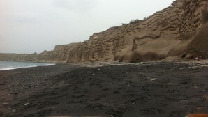 Een strand met donker zand en een rotsachtige klif.