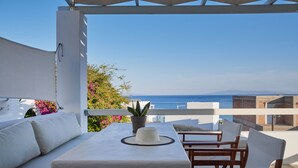 A terrace with a white table and chairs, a potted plant, and a view of the sea.