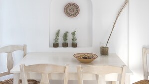A white dining table with four chairs, a decorative plate, and three small potted plants on a white wall.