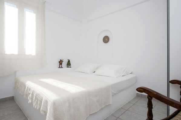 Un dormitorio blanco con una cama, una pequeña decoración en la pared y una ventana.