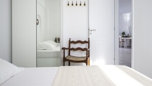 A bedroom with a bed, a wooden chair, a wardrobe, and a door with a coat rack.