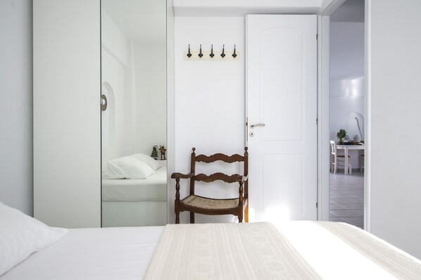 A bedroom with a bed, a wooden chair, a wardrobe, and a door with a coat rack.