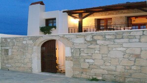 A stone wall with an arched entrance leading to a building with a balcony.
