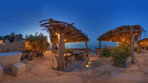 A beachside restaurant with outdoor seating, stone walls, and string lights.
