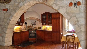 A rustic kitchen with stone walls, wooden cabinets, and a stone archway.