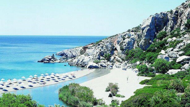 A coastal beach with a rocky cliff, a sandy beach, and a clear blue sea.