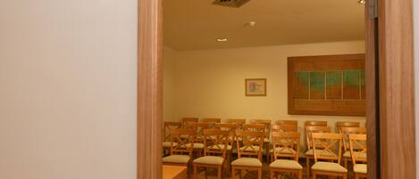 A room with wooden chairs arranged in rows, a wooden table, and a painting on the wall.