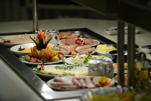 A buffet with various dishes including meats, cheeses, and vegetables.
