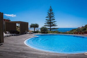 A swimming pool with a wooden deck, lounge chairs, and a tall pine tree. - Hotel do Campo (Ribeira Brava)