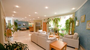 Een ruime lobby met een beige bank, een houten tafel en verschillende potplanten.